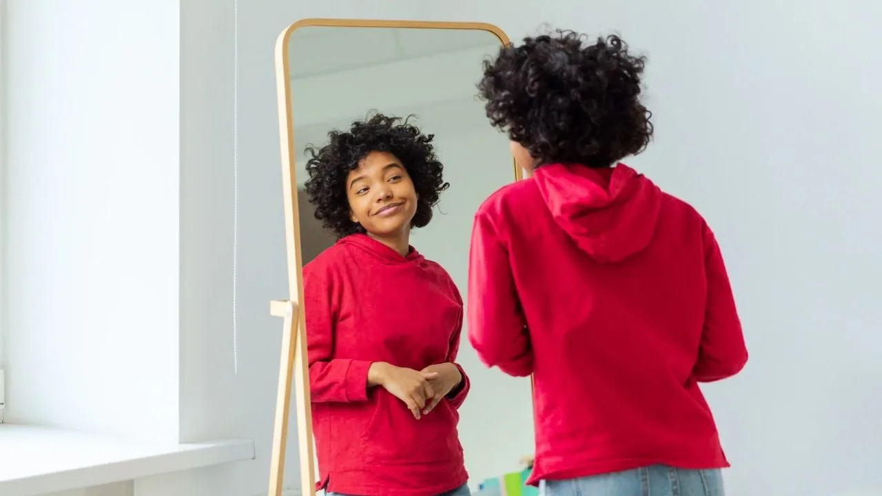Self love: young lady in red sweater smiling at her reflection in the mirror